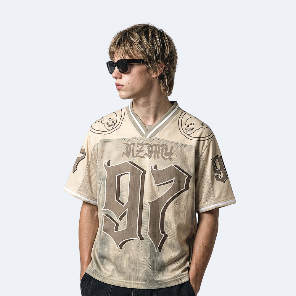 Beige. A model wearing a beige and brown vintage-style hockey jersey with Necro and the number 97 on the front, styled with black sunglasses.