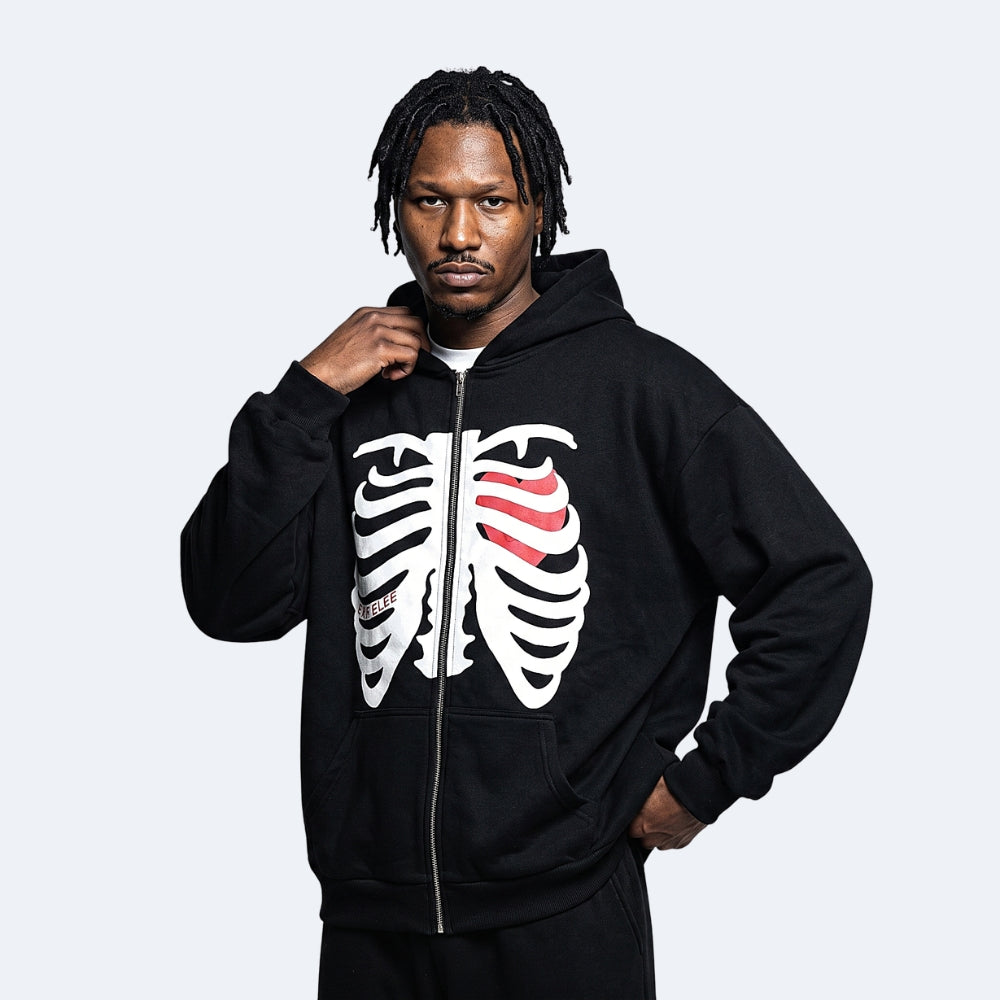 Black. A man wearing a black zip-up hoodie with a white rib cage graphic and a red striped accent on the chest.