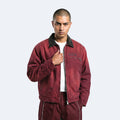 A man wearing a distressed maroon bomber jacket with a black corduroy collar, a white t-shirt, and matching maroon pants, standing against a light gray background.