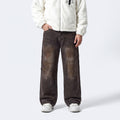 A person wearing loose, wide-leg brown distressed jeans with diagonal seam details, paired with a cream fleece jacket and white sneakers, shown from the chest down on a light gray studio background.
