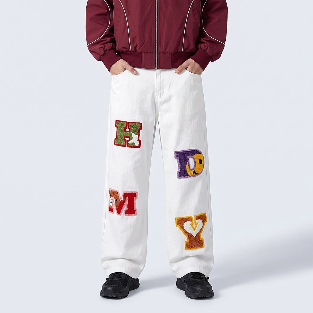 White. A person wearing white wide-leg pants with colorful embroidered varsity letters on the front, paired with a burgundy zip-up jacket and black sneakers.