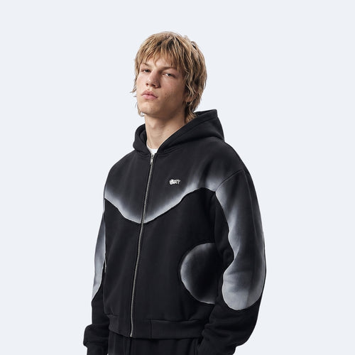 A model wearing a black zip-up hoodie with a gray gradient abstract pattern on the chest and sleeves, set against a light gray studio background.