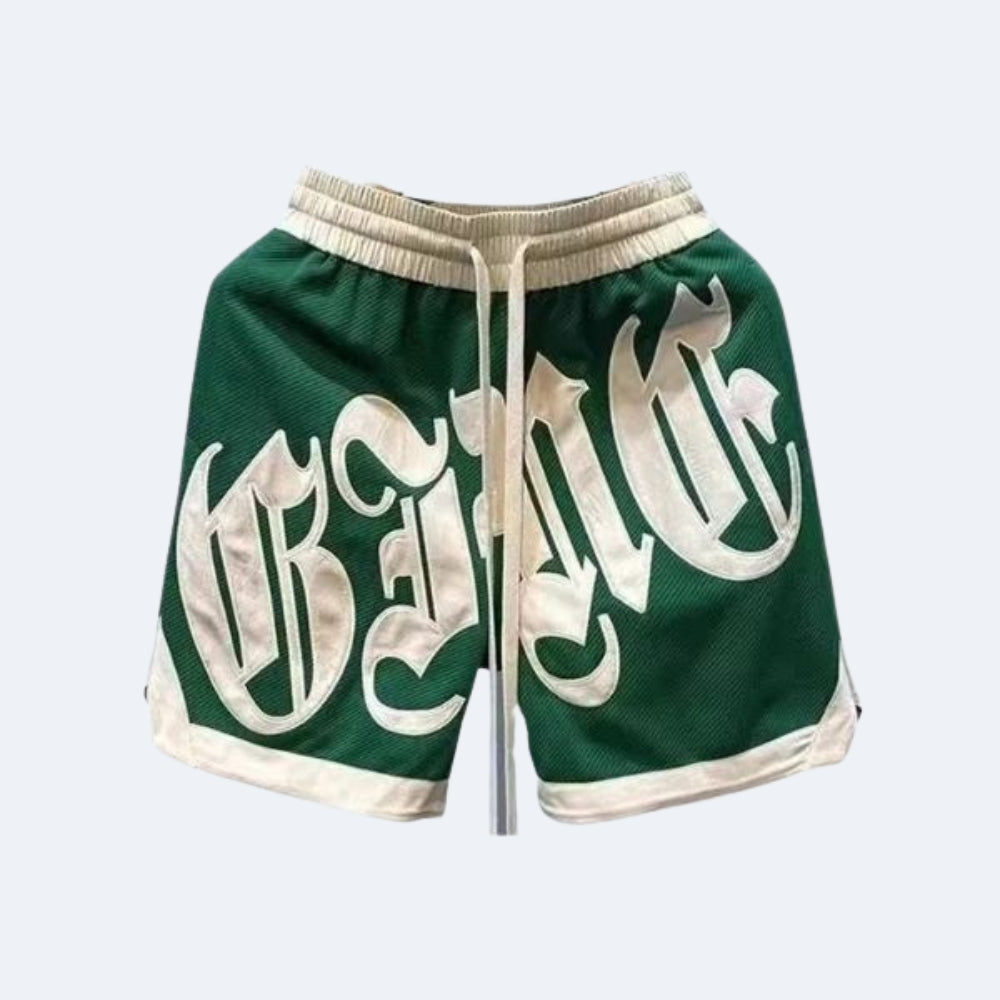 Green. Green mesh basketball shorts with a large white Gothic-style graphic on the front, featuring a cream-colored drawstring and trim.