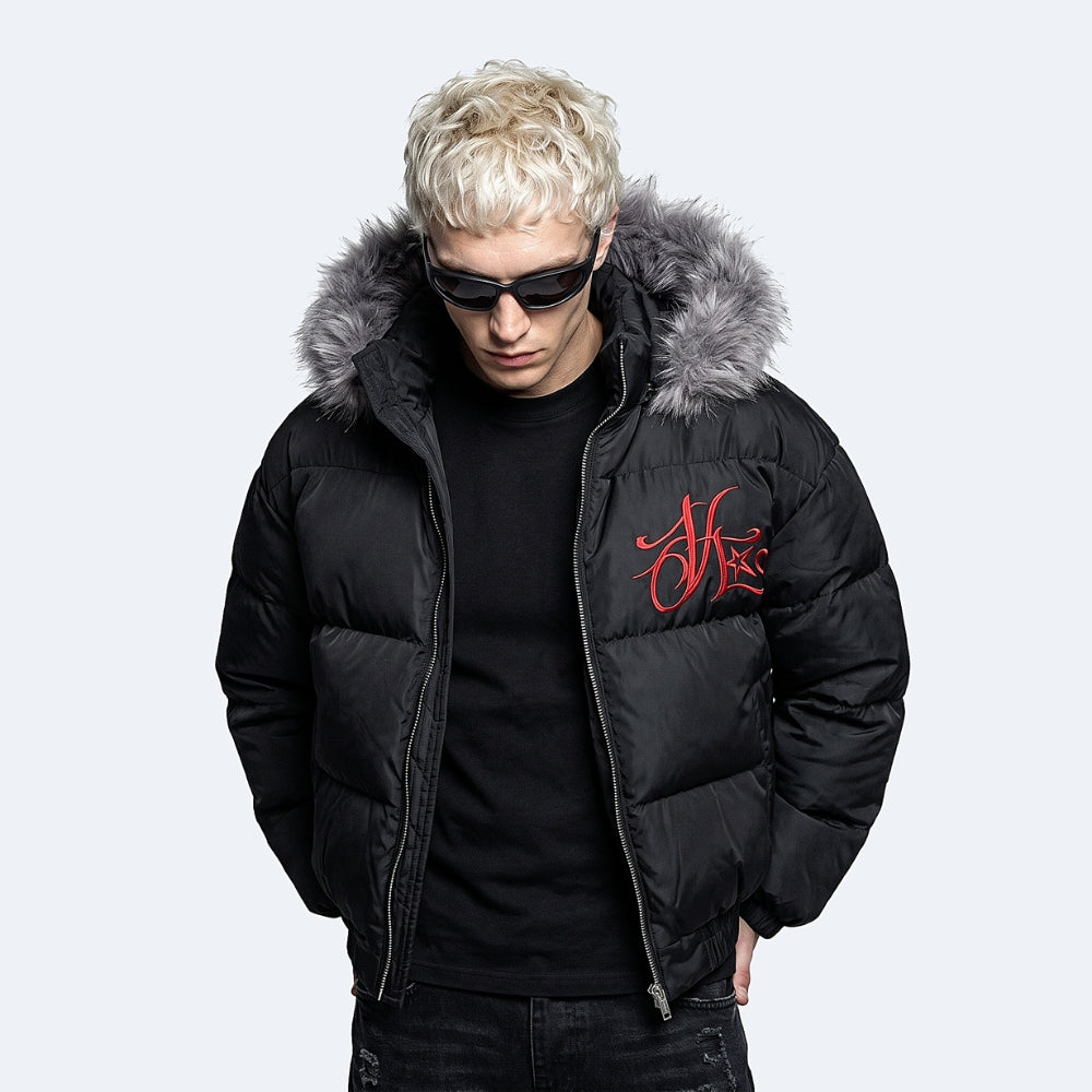 A man wearing a black puffer jacket with a gray faux-fur trimmed hood and a red embroidered logo on the chest, set against a light gray background.
