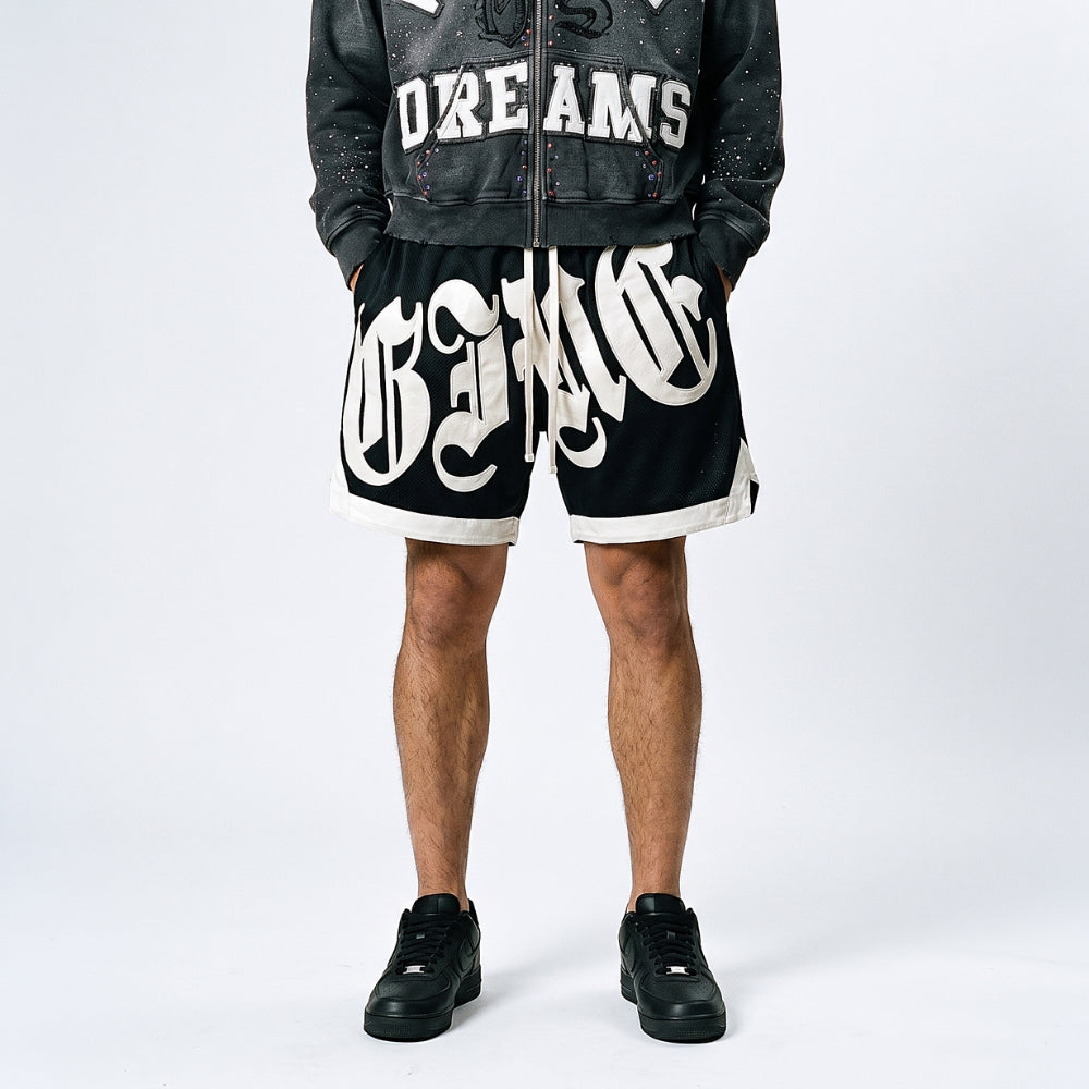 Black. A model shown from the waist down wearing black shorts with a large white gothic-style graphic print, a black distressed zip-up jacket, and black sneakers.