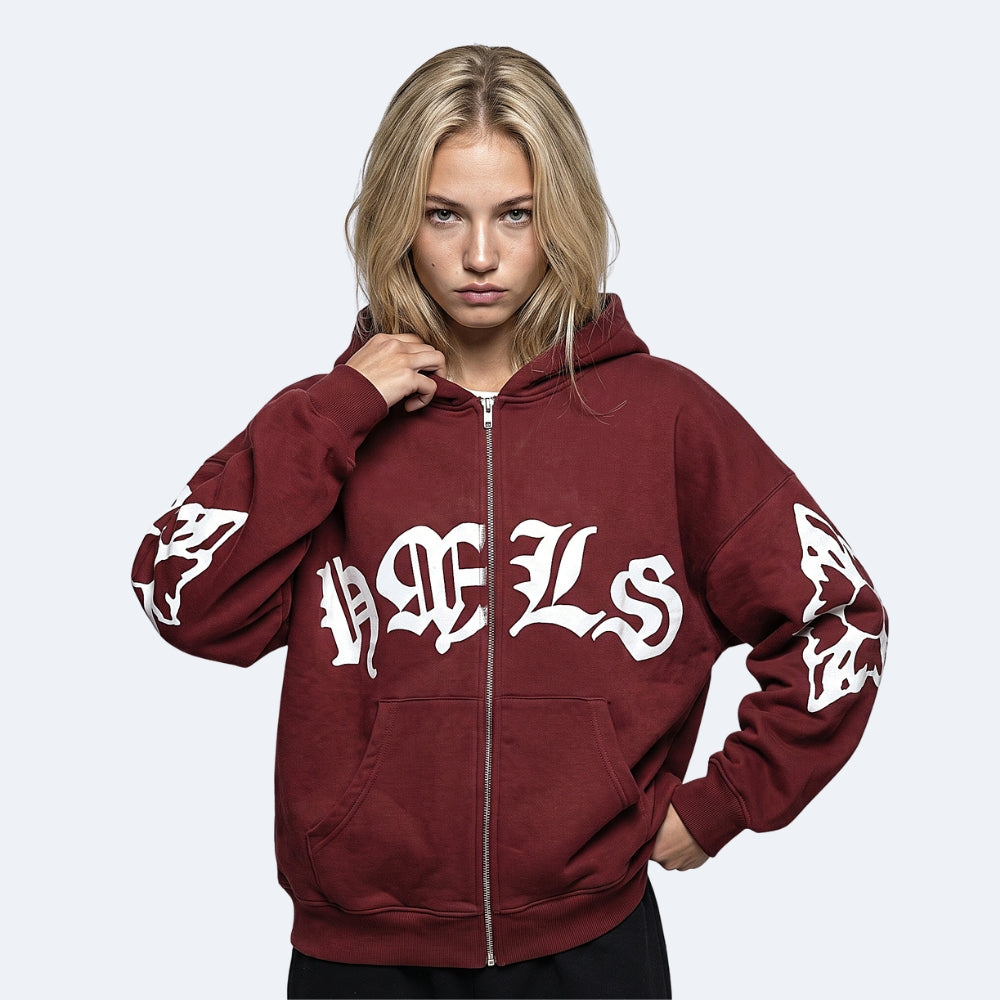 Burgundy. A woman wearing a burgundy zip-up hoodie with white Gothic lettering on the front and sleeves.