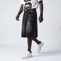 A model wearing black washed denim shorts, a white graphic t-shirt, and white sneakers, shown from the chest down against a light gray studio background.