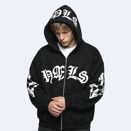 A person wearing a black zip-up hoodie with large white Gothic-style lettering across the chest, hood, and sleeves, photographed against a light gray studio background.