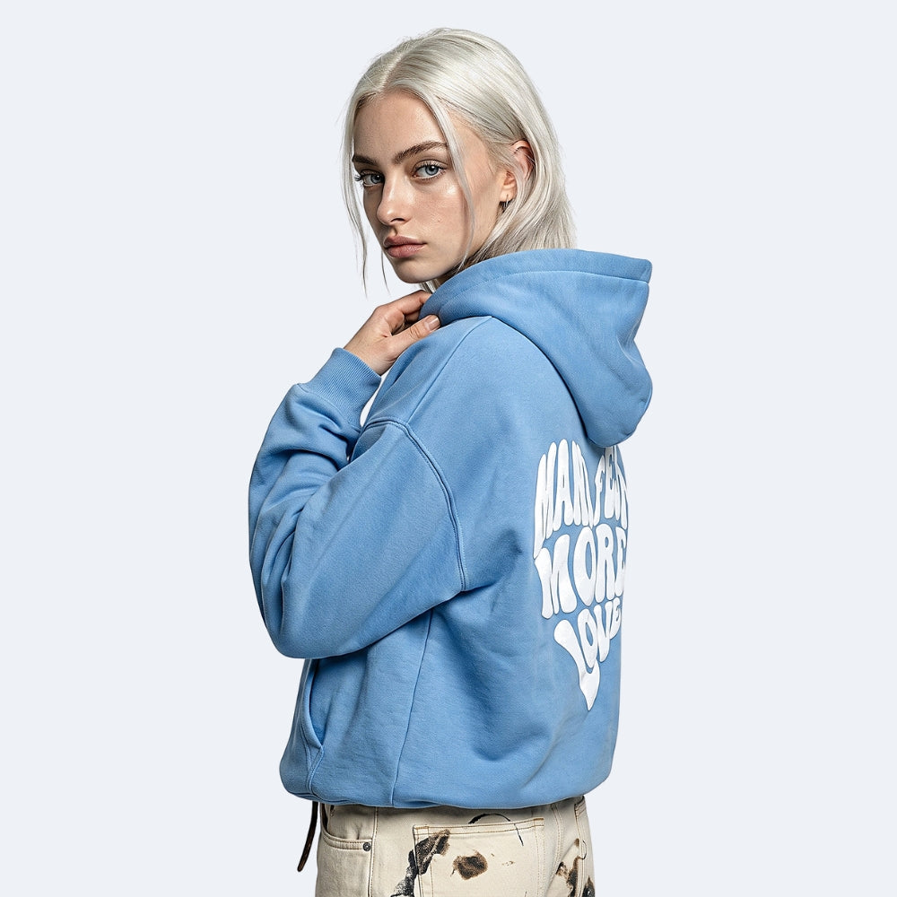 Blue. A model with platinum blonde hair wearing a light blue cropped hoodie with white graphic text on the back, paired with beige pants.