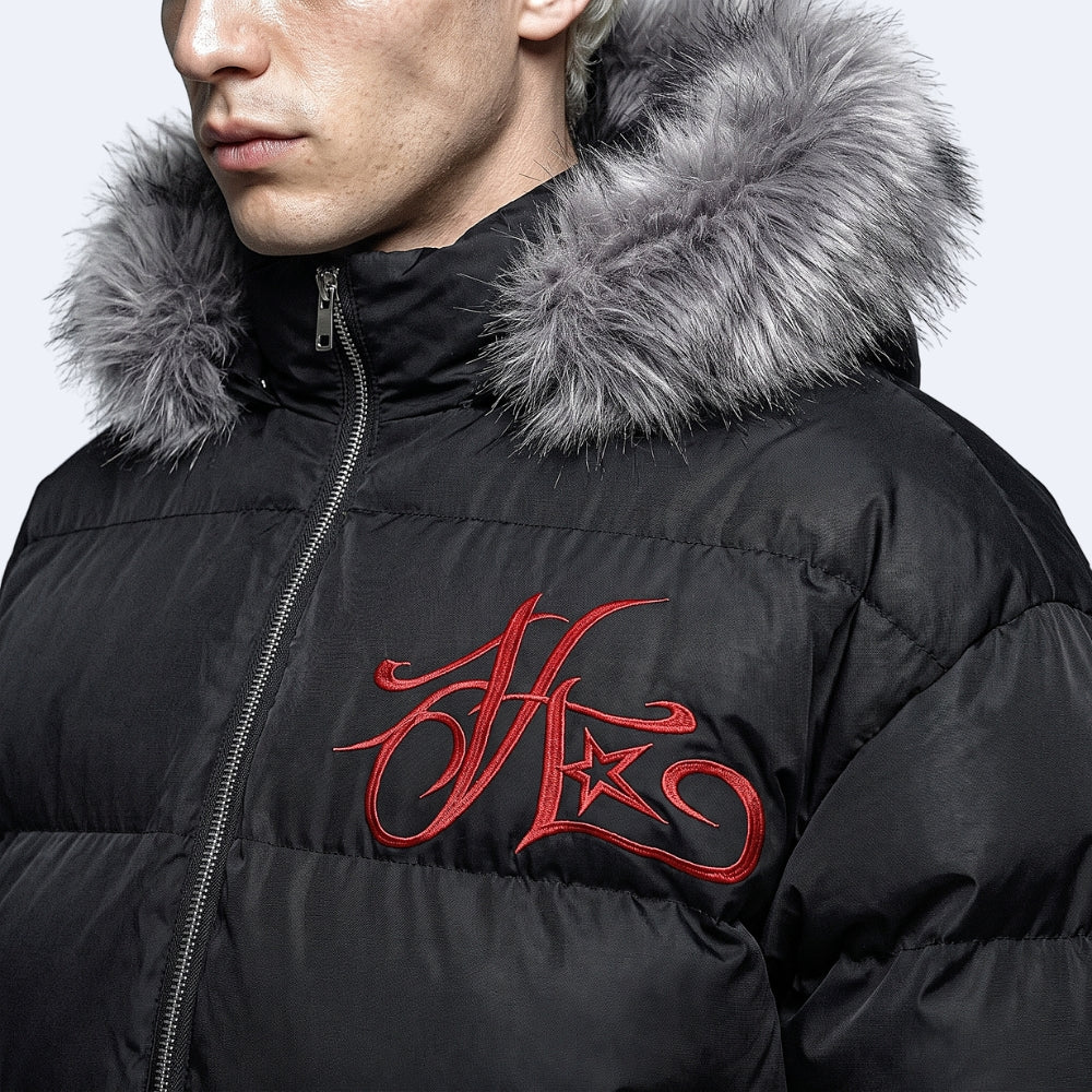 Close-up of a person wearing a black puffer jacket with a gray faux-fur hood trim and a red embroidered stylized logo on the chest.