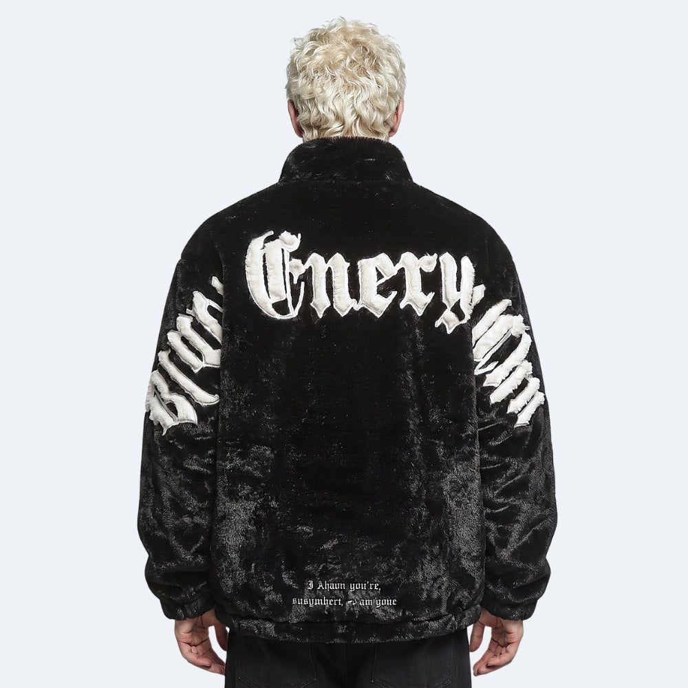 A person shown from the back wearing a black velour jacket with large white Gothic-style lettering across the upper back and curved white lettering down both sleeves, against a light gray studio background.