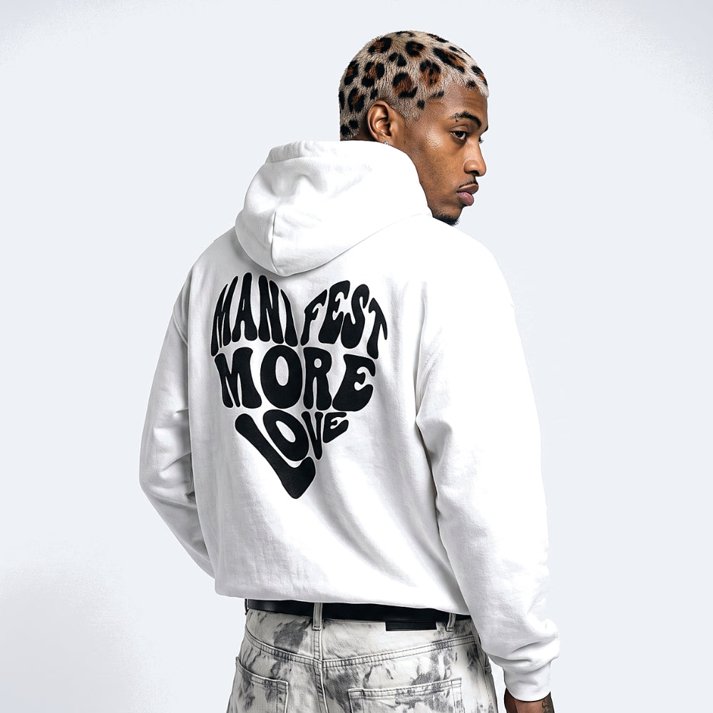 White. A man shown from the back wearing a white pullover hoodie with a large black graphic text reading MANIFEST MORE LOVE, paired with light gray jeans.