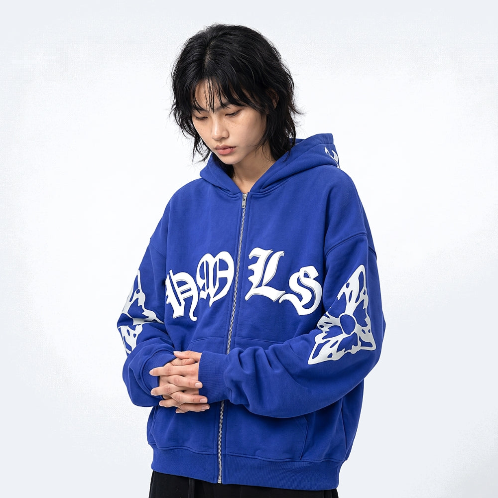 A model wearing a royal blue zip-up hoodie with white gothic-style lettering and sleeve graphics, set against a plain light gray background.