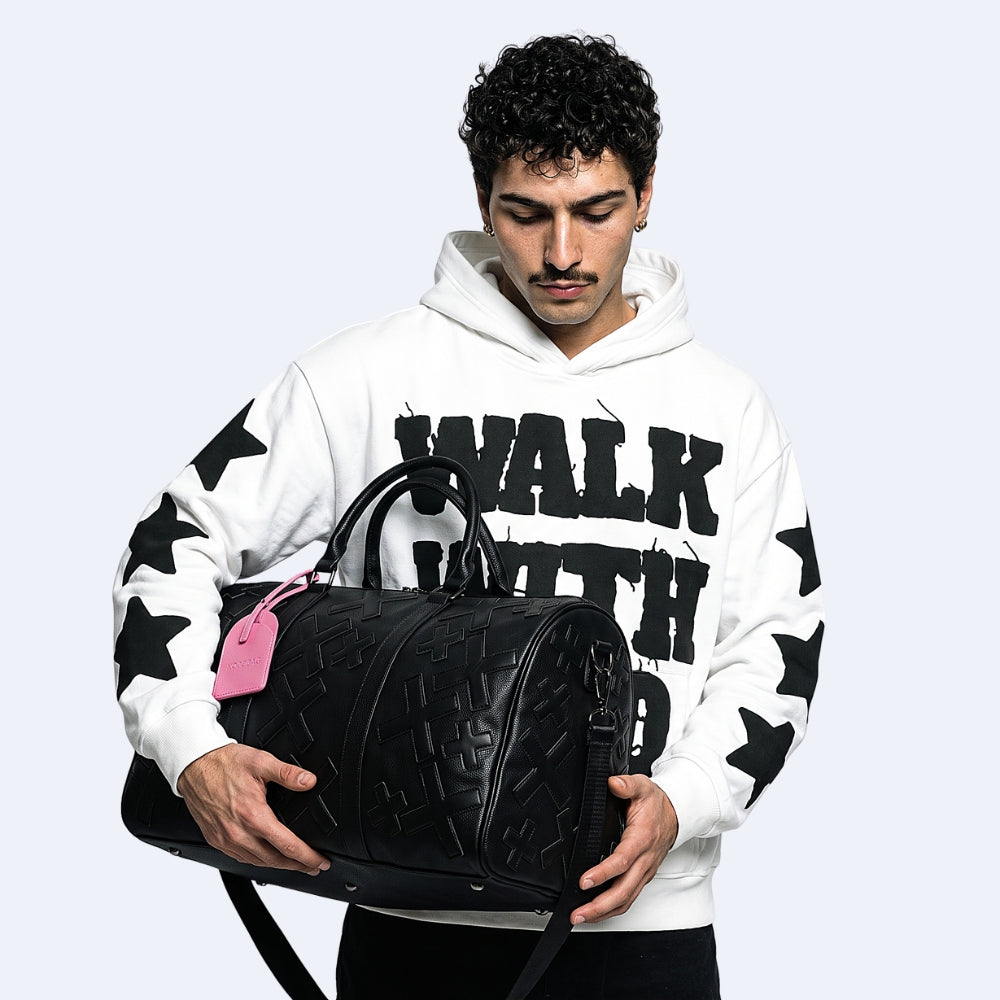 Black. KRUX Crossover duffle bag in black embossed leather, carried by a model in a white hoodie