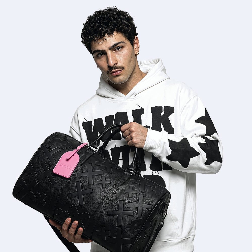 Black. KRUX Crossover duffle bag in black, held by a model — embossed finish with pink luggage tag