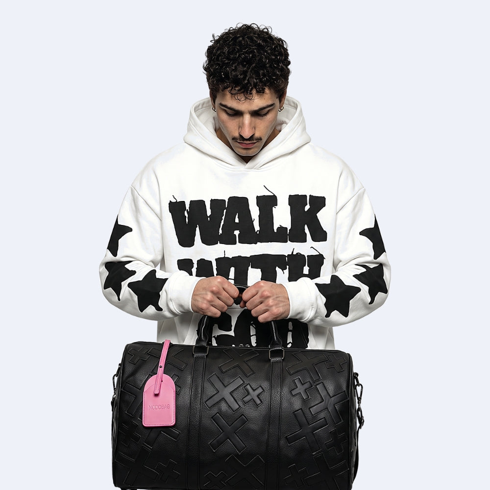 Black. KRUX Crossover duffle bag in black embossed monogram, held by a model with a pink luggage tag