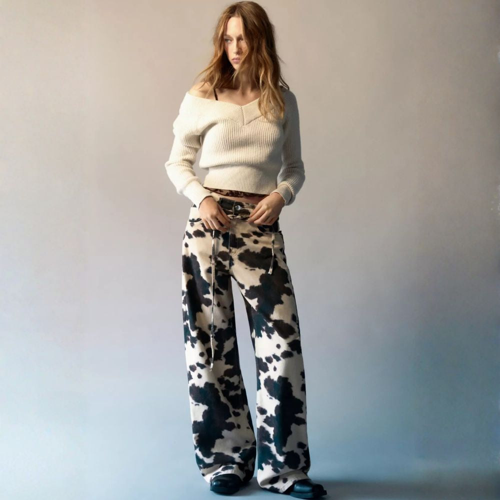 Woman wearing a white sweater and patterned pants against a plain background