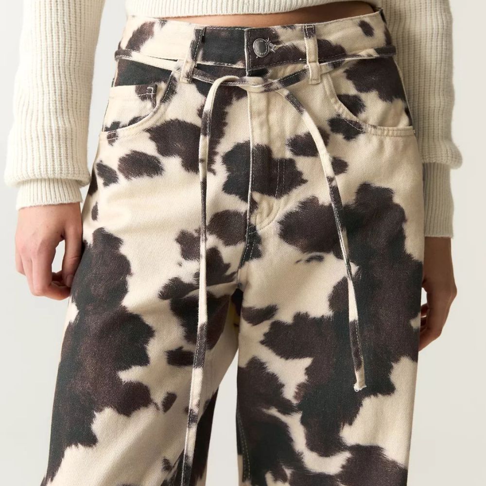 Cow print pants worn by a person on a plain background