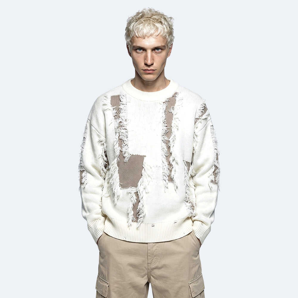 White. A model with platinum blonde hair wearing a cream-colored distressed knit sweater with brown patches and beige cargo pants.