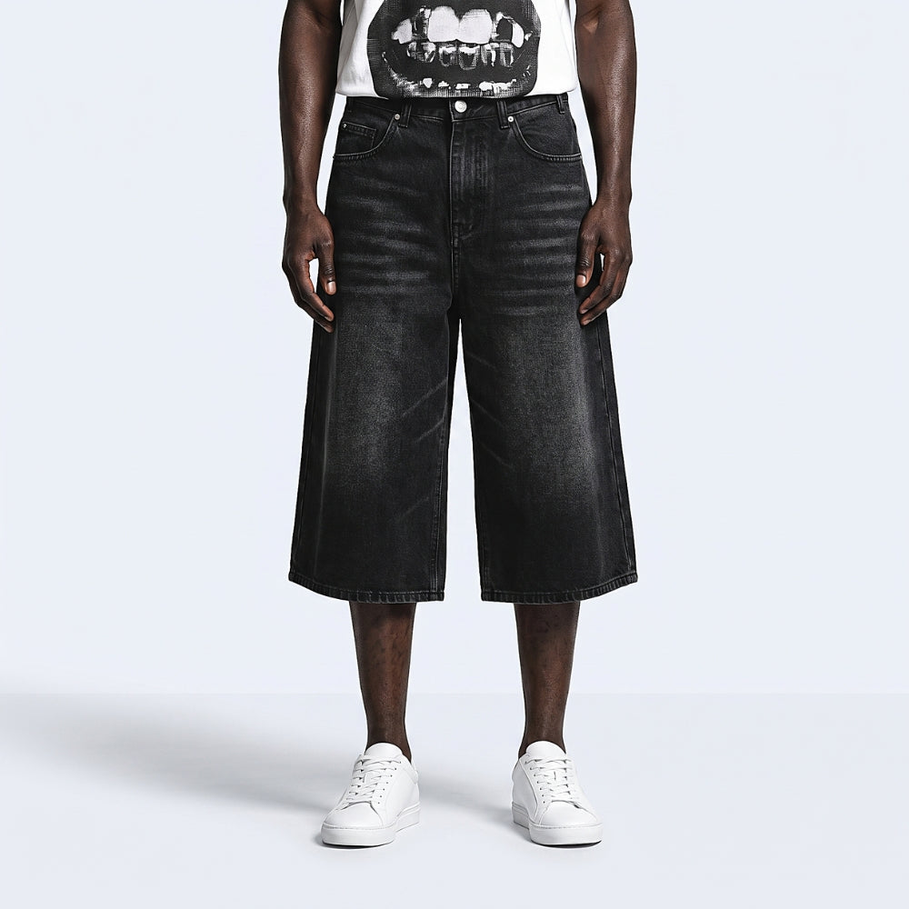 A model wearing black wide-leg cropped denim shorts, styled with a white graphic t-shirt and white sneakers, photographed against a light gray studio background.