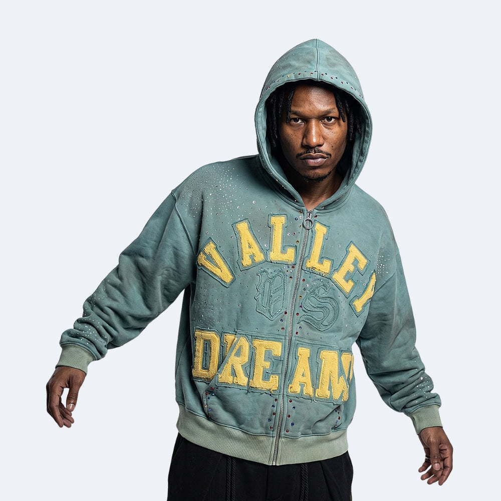 Cyan. A man wearing a distressed sage-green zip-up hoodie with yellow text on the front.